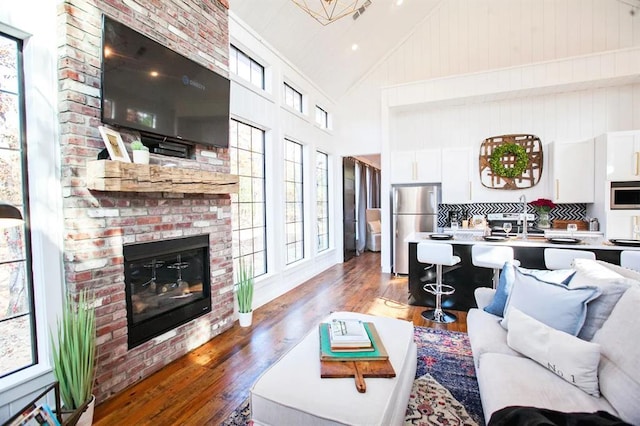 living room with high vaulted ceiling, a brick fireplace, and light wood-type flooring