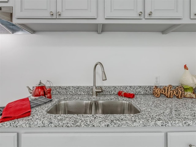 kitchen with white cabinets, light stone counters, and sink