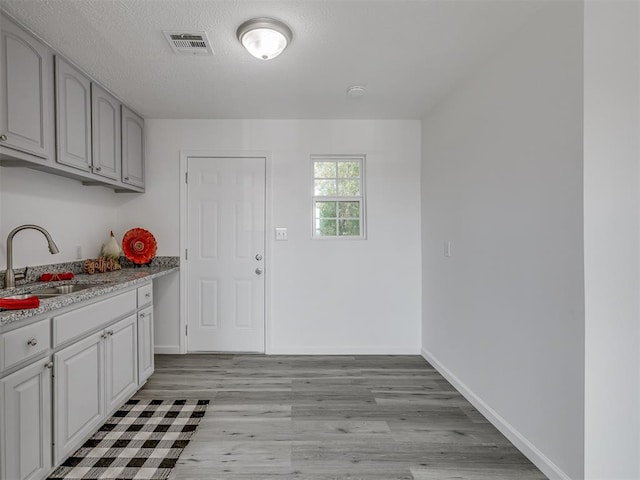 kitchen featuring a textured ceiling, light stone counters, sink, and light hardwood / wood-style flooring