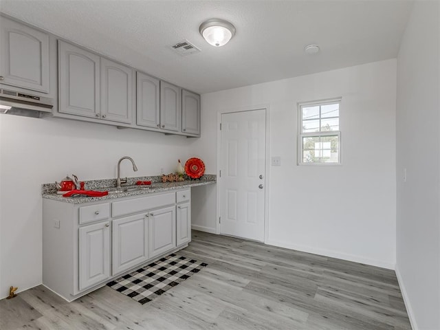 kitchen featuring a textured ceiling, light wood-type flooring, range hood, and sink