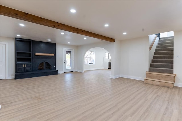 unfurnished living room featuring beam ceiling, a large fireplace, and light hardwood / wood-style floors