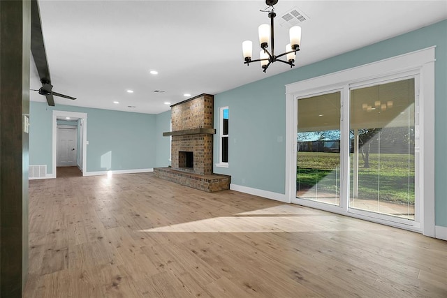 unfurnished living room with ceiling fan with notable chandelier, a fireplace, and light hardwood / wood-style flooring