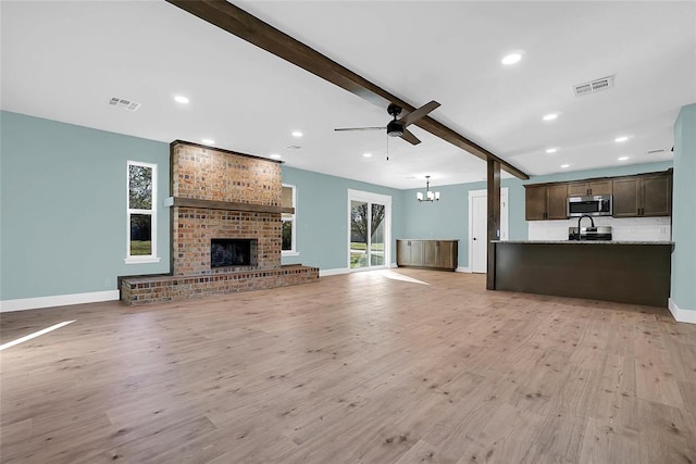 unfurnished living room with beamed ceiling, ceiling fan with notable chandelier, light hardwood / wood-style floors, and a fireplace