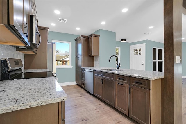 kitchen with light stone counters, light wood-type flooring, sink, and appliances with stainless steel finishes