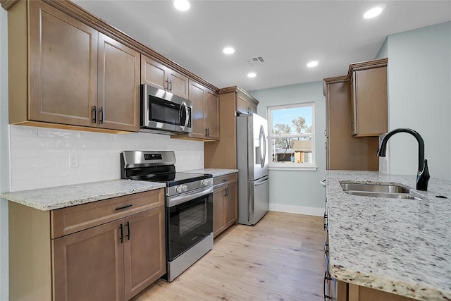 kitchen with light stone countertops, appliances with stainless steel finishes, backsplash, sink, and light hardwood / wood-style flooring