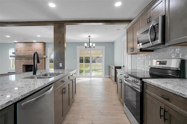 kitchen with sink, hanging light fixtures, light wood-type flooring, appliances with stainless steel finishes, and light stone counters