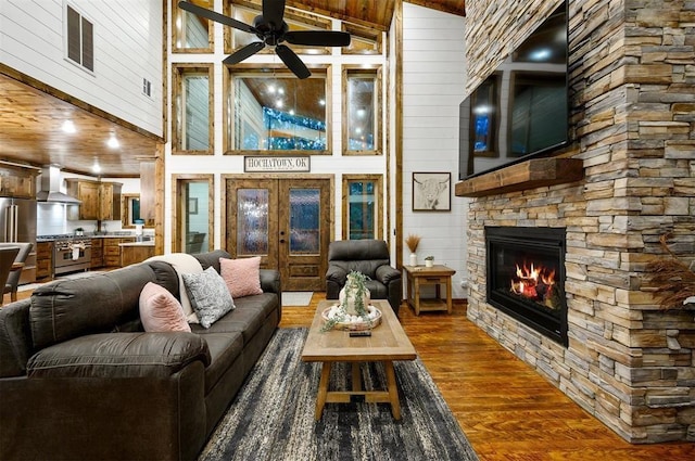 living room featuring a stone fireplace, wood walls, hardwood / wood-style floors, and ceiling fan