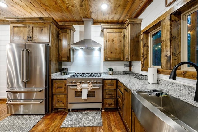 kitchen with wall chimney exhaust hood, high quality appliances, sink, and dark wood-type flooring