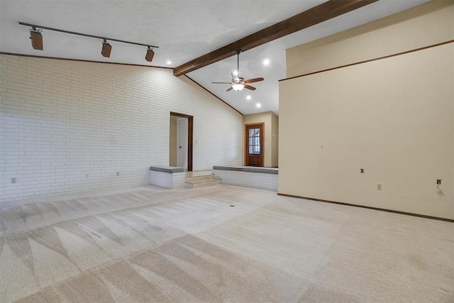 empty room featuring track lighting, ceiling fan, beam ceiling, light colored carpet, and brick wall