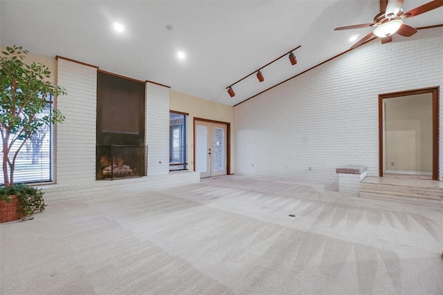 unfurnished living room featuring light carpet, french doors, rail lighting, ceiling fan, and a fireplace