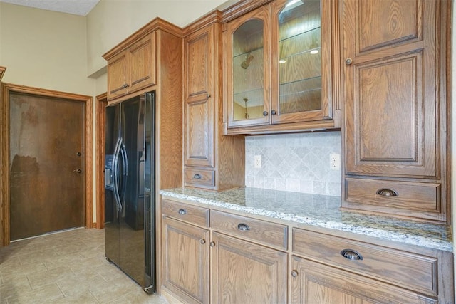 kitchen featuring backsplash, black fridge, light tile patterned flooring, and light stone countertops