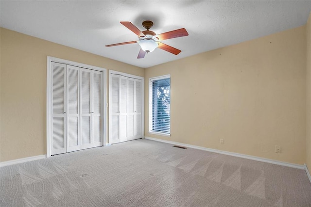 unfurnished bedroom with a textured ceiling, ceiling fan, light carpet, and two closets