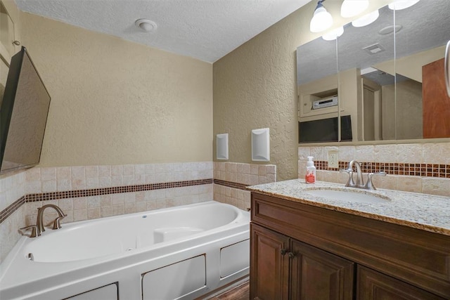 bathroom with a washtub, vanity, a textured ceiling, and decorative backsplash