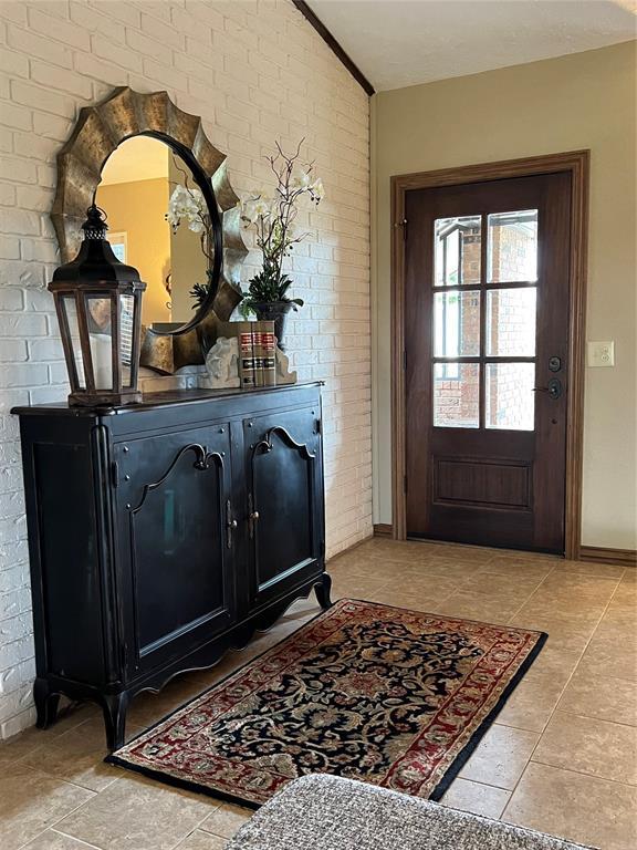 foyer featuring light tile patterned floors, brick wall, and lofted ceiling