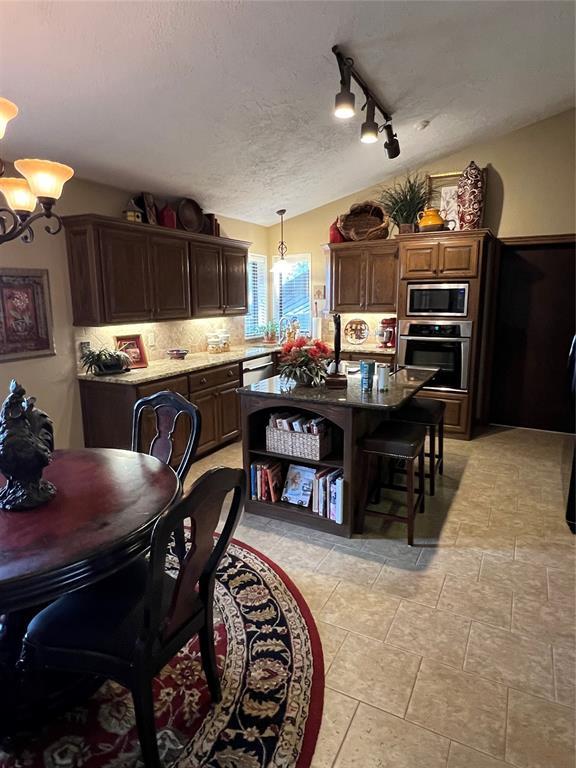 kitchen featuring appliances with stainless steel finishes, dark brown cabinets, a textured ceiling, pendant lighting, and a notable chandelier