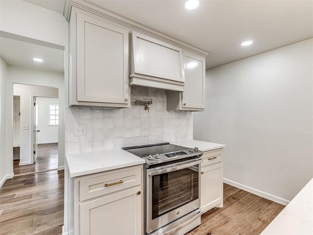 kitchen featuring hardwood / wood-style floors, custom exhaust hood, electric stove, decorative backsplash, and light stone counters