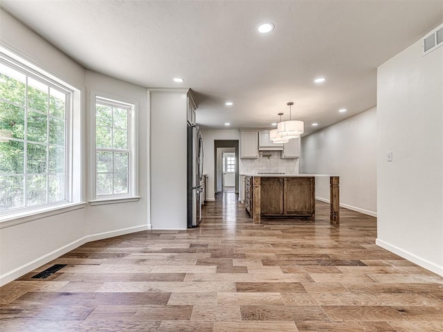 kitchen featuring pendant lighting, decorative backsplash, light hardwood / wood-style floors, a kitchen island, and stainless steel refrigerator