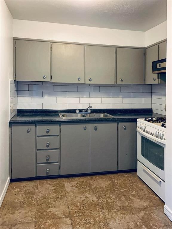 kitchen featuring decorative backsplash, white gas range oven, gray cabinets, and sink