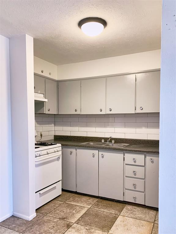 kitchen with gray cabinetry, white stove, sink, a textured ceiling, and tasteful backsplash