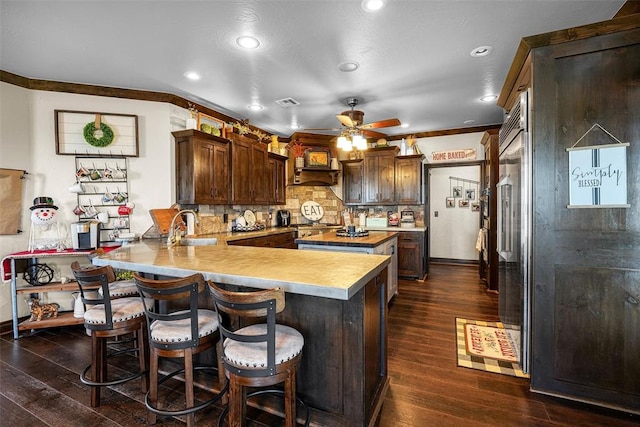 kitchen featuring sink, dark wood-type flooring, kitchen peninsula, a breakfast bar, and ornamental molding