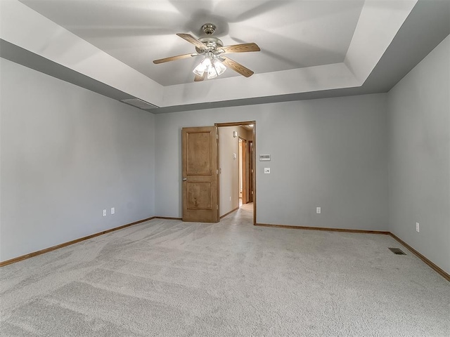 empty room with ceiling fan, a tray ceiling, and light carpet