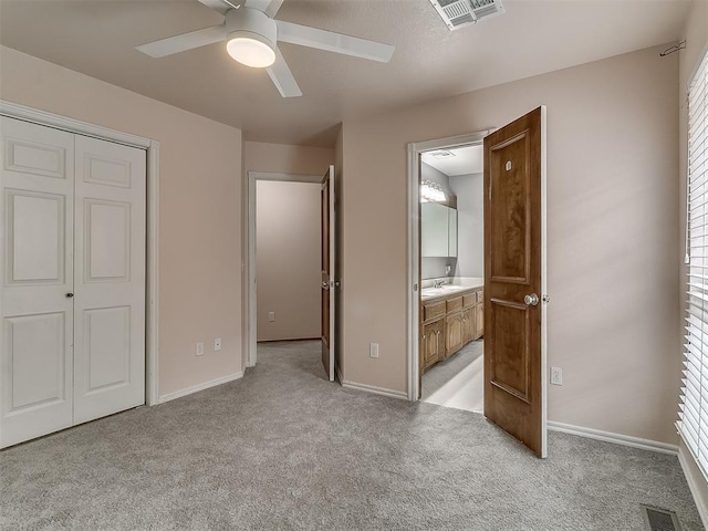 unfurnished bedroom with ceiling fan, connected bathroom, a closet, light colored carpet, and sink