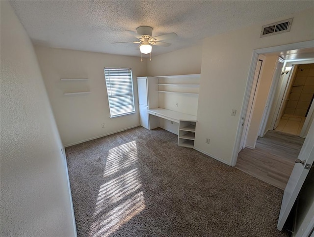 unfurnished bedroom featuring ceiling fan, light colored carpet, and a textured ceiling