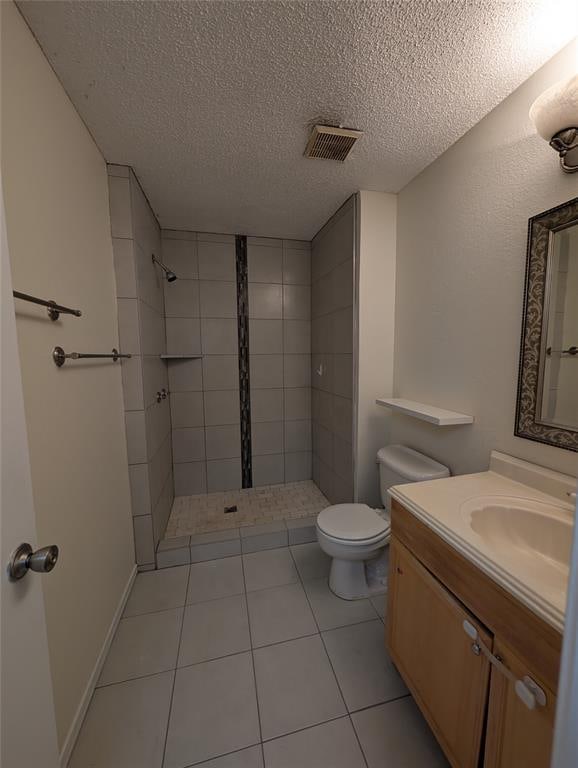 bathroom with vanity, tile patterned floors, toilet, a textured ceiling, and a tile shower