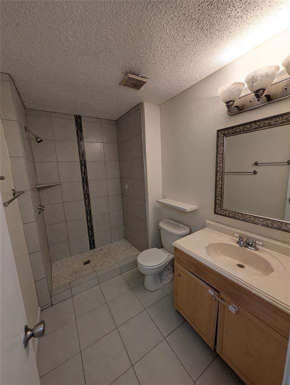 bathroom with vanity, tile patterned floors, toilet, tiled shower, and a textured ceiling