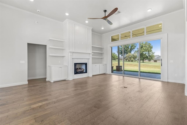 unfurnished living room featuring crown molding, a tiled fireplace, a ceiling fan, and wood finished floors