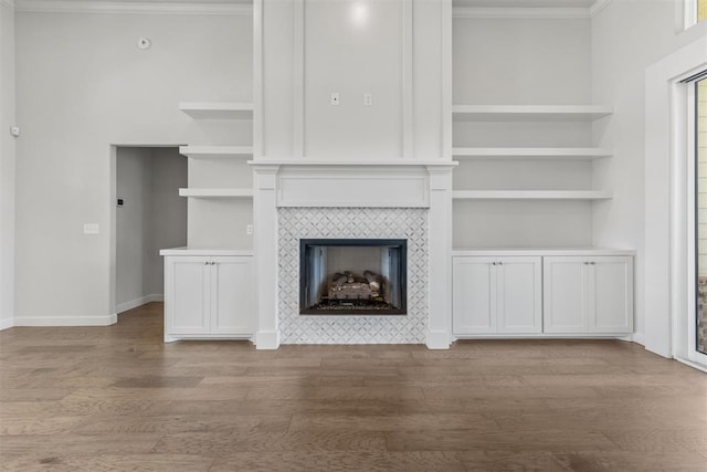 unfurnished living room featuring baseboards, ornamental molding, a tiled fireplace, and wood finished floors