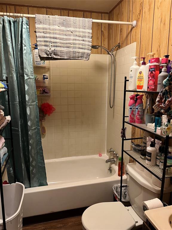 bathroom with hardwood / wood-style flooring, toilet, shower / bath combo with shower curtain, and wooden walls