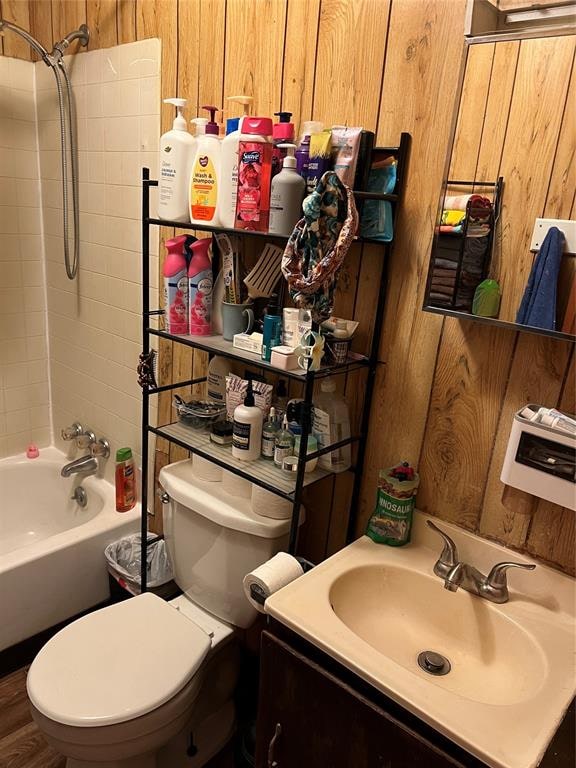 full bathroom featuring shower / bathtub combination, vanity, hardwood / wood-style flooring, toilet, and wood walls