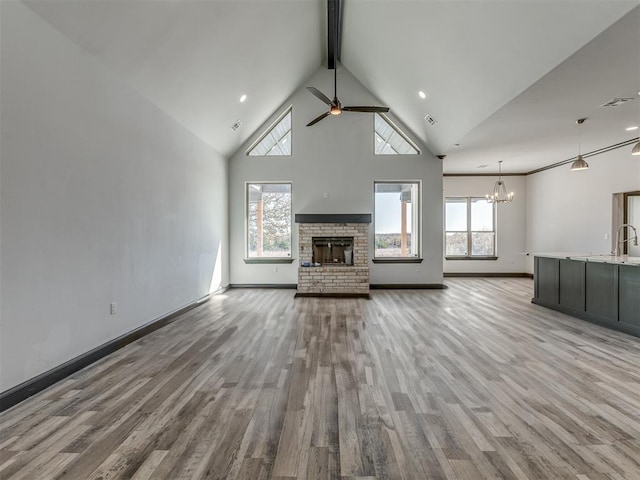 unfurnished living room with a fireplace, ceiling fan with notable chandelier, light hardwood / wood-style floors, and plenty of natural light