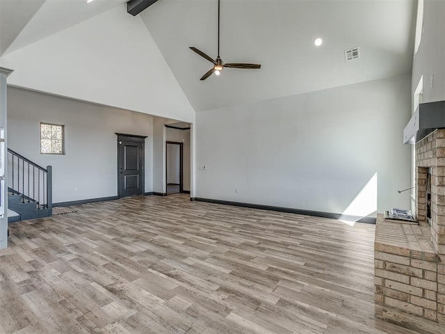 unfurnished living room featuring ceiling fan, beam ceiling, high vaulted ceiling, a fireplace, and light hardwood / wood-style floors