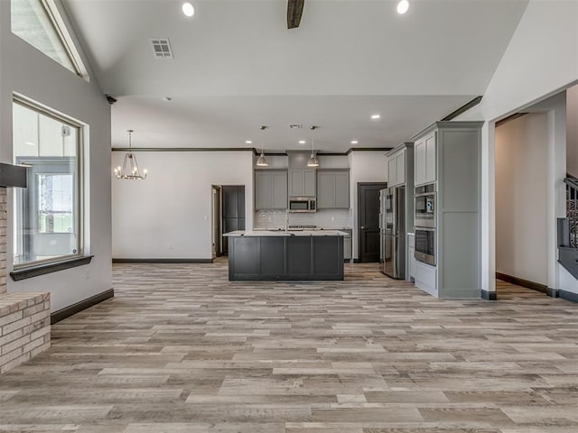 kitchen featuring vaulted ceiling, gray cabinets, an island with sink, appliances with stainless steel finishes, and decorative light fixtures