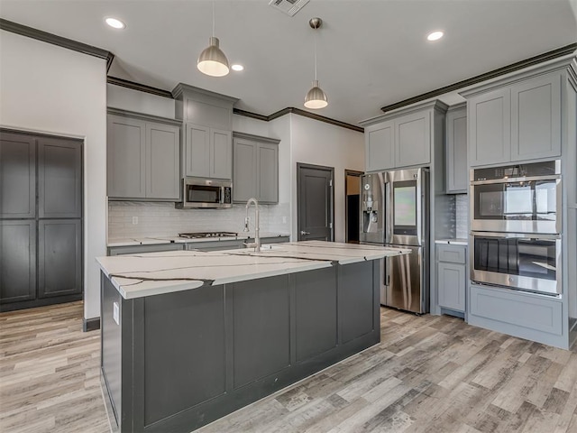 kitchen with light stone counters, pendant lighting, stainless steel appliances, and light wood-type flooring