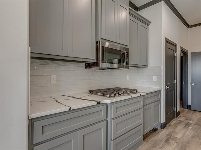 kitchen featuring decorative backsplash, light wood-type flooring, ornamental molding, appliances with stainless steel finishes, and light stone counters