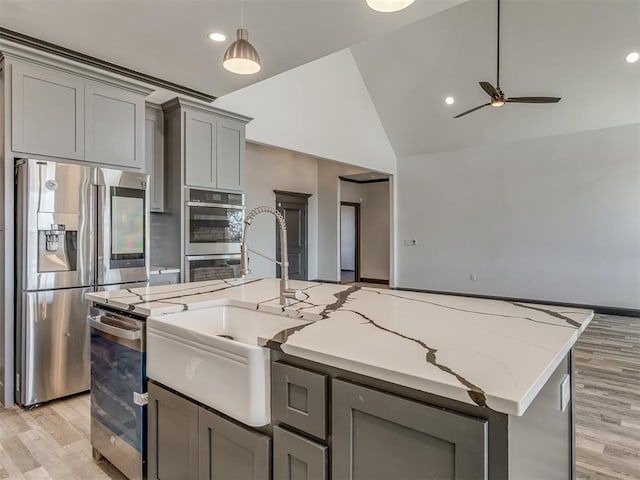 kitchen featuring ceiling fan, light stone counters, light hardwood / wood-style flooring, vaulted ceiling, and appliances with stainless steel finishes