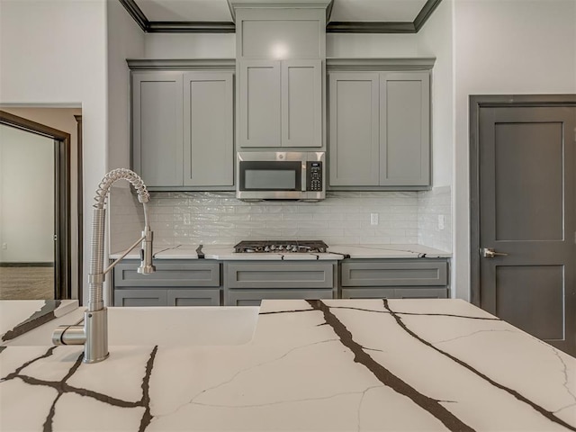 kitchen with appliances with stainless steel finishes, tasteful backsplash, light stone counters, ornamental molding, and gray cabinets