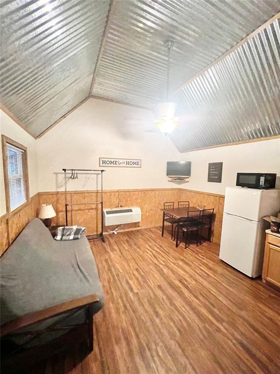 interior space with white refrigerator, a wall unit AC, wood walls, wood-type flooring, and lofted ceiling