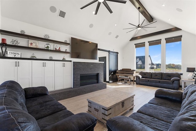 living room featuring a brick fireplace, a barn door, beamed ceiling, high vaulted ceiling, and light hardwood / wood-style floors