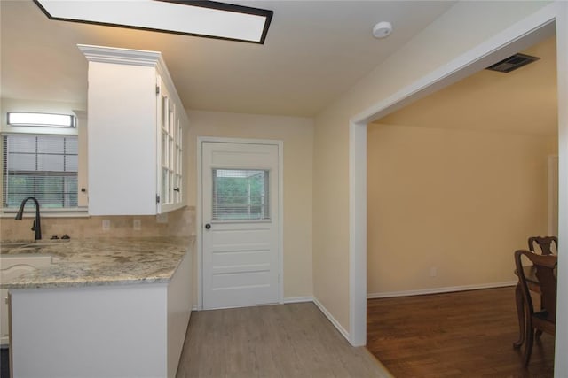 kitchen with white cabinets, sink, decorative backsplash, light stone countertops, and light wood-type flooring