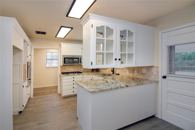 kitchen with white cabinets, light hardwood / wood-style flooring, appliances with stainless steel finishes, tasteful backsplash, and kitchen peninsula