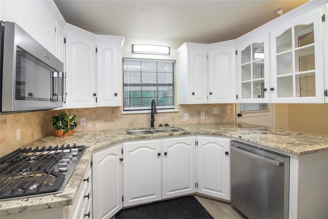 kitchen featuring appliances with stainless steel finishes, backsplash, light stone counters, sink, and white cabinetry