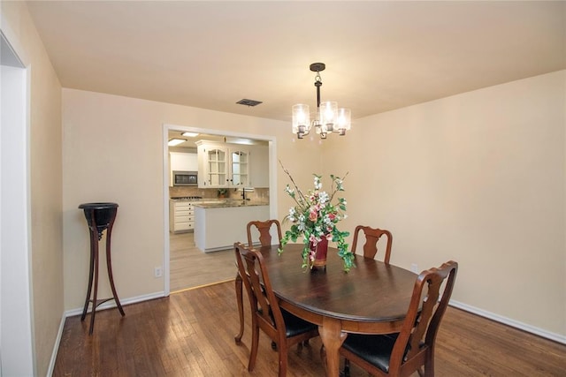 dining space featuring sink, wood-type flooring, and a notable chandelier