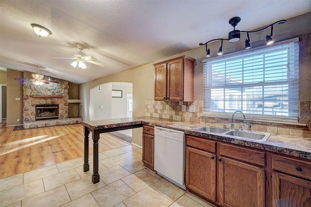 kitchen with sink, white dishwasher, decorative backsplash, a fireplace, and light wood-type flooring