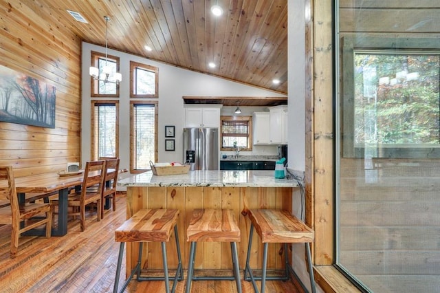 kitchen with white cabinetry, light stone counters, stainless steel refrigerator with ice dispenser, kitchen peninsula, and a kitchen bar