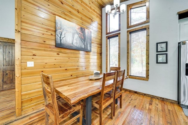 dining space featuring an inviting chandelier, light hardwood / wood-style flooring, and wooden walls