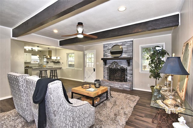 living room featuring ceiling fan, a brick fireplace, beamed ceiling, dark hardwood / wood-style floors, and crown molding